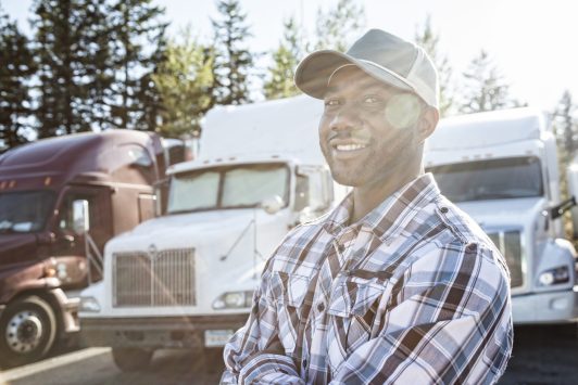 Black man truck driver near his truck parked in a parking lot at a truck stop